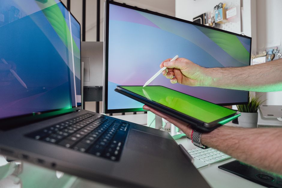 Osoba koristi stylus na tabletu u tehnološkom radnom prostoru s dvostrukim monitorima